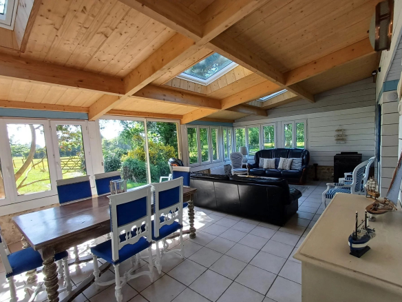 Intérieur d'une véranda lumineuse avec des meubles en bois et des fenêtres donnant sur un jardin.