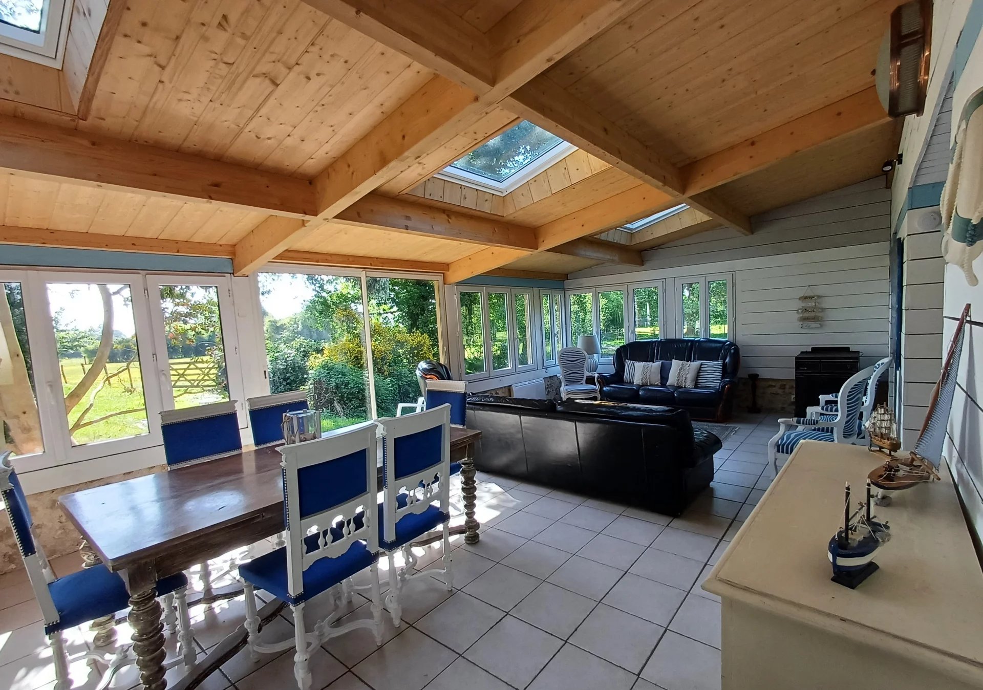 Intérieur d'une véranda lumineuse avec des meubles en bois et des fenêtres donnant sur un jardin.