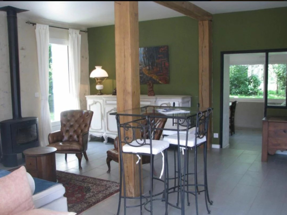 Intérieur d'une maison avec un coin salon et une table haute, dans un cadre naturel.