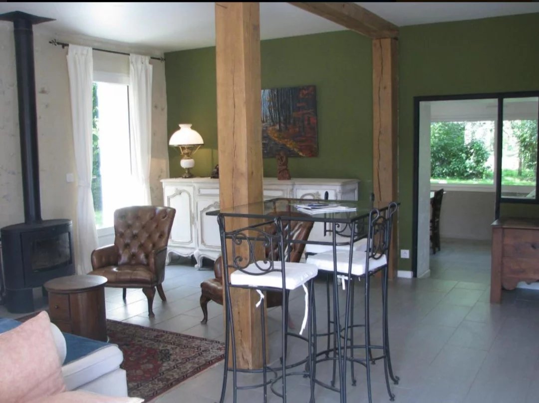 Intérieur d'une maison avec un coin salon et une table haute, dans un cadre naturel.