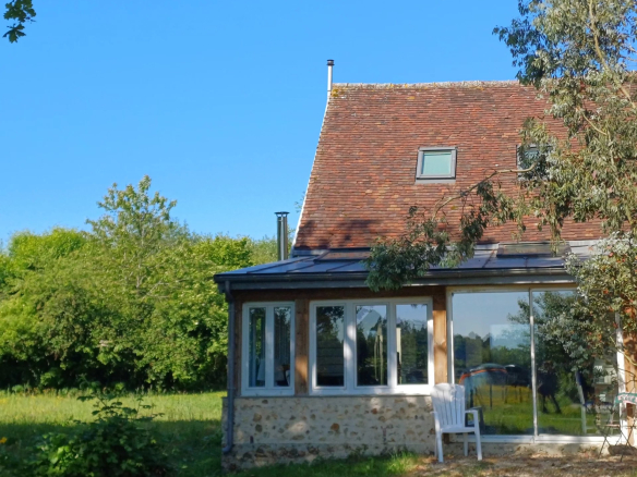 Maison avec toit en ardoise et véranda, entourée d'un parc verdoyant dans le Parc Naturel Régional du Perche.