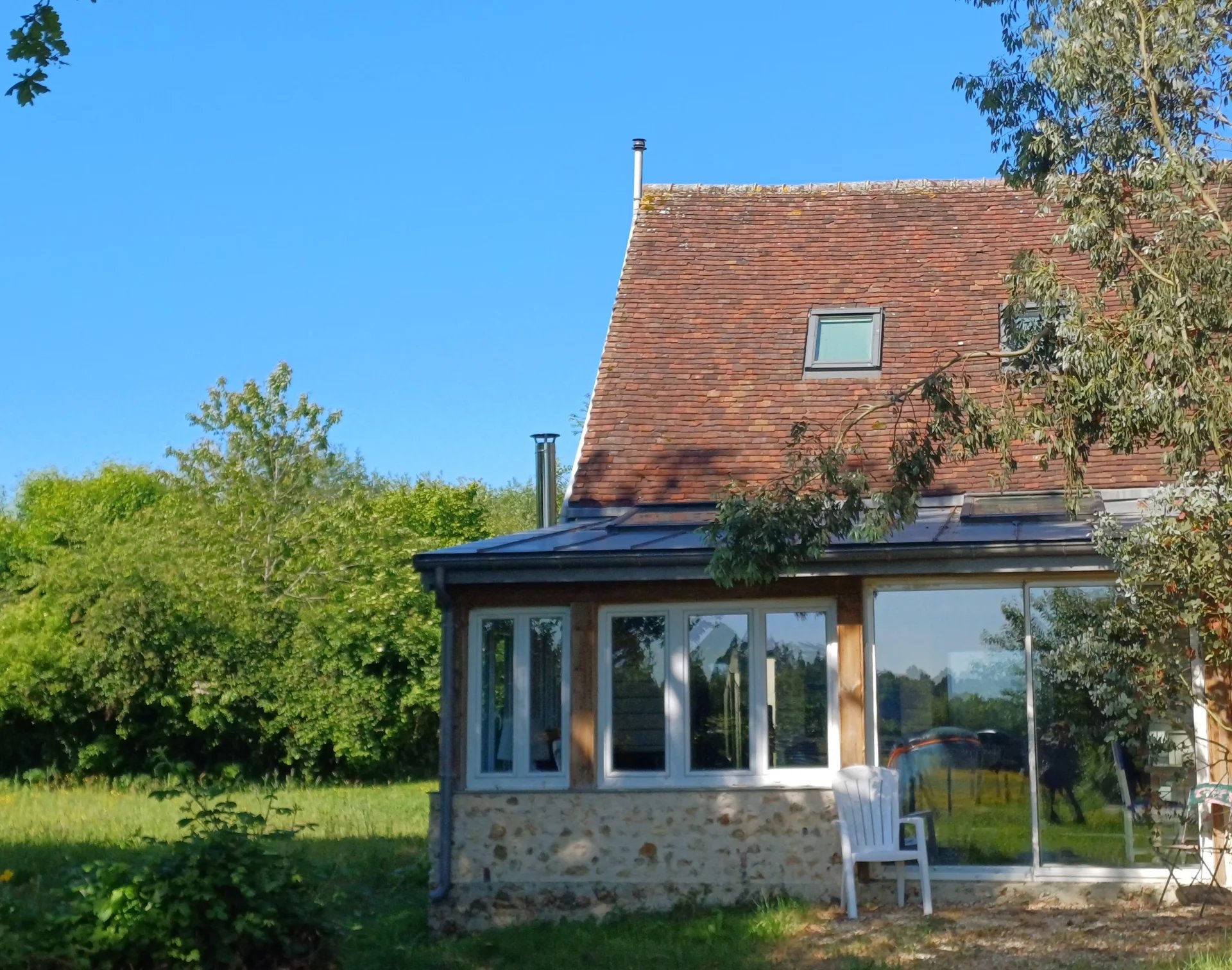 Maison avec toit en ardoise et véranda, entourée d'un parc verdoyant dans le Parc Naturel Régional du Perche.