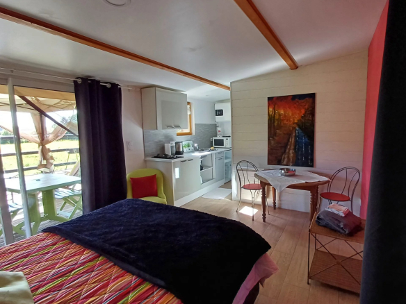 Intérieur d'un logement avec cuisine et coin salon, vue sur un jardin.