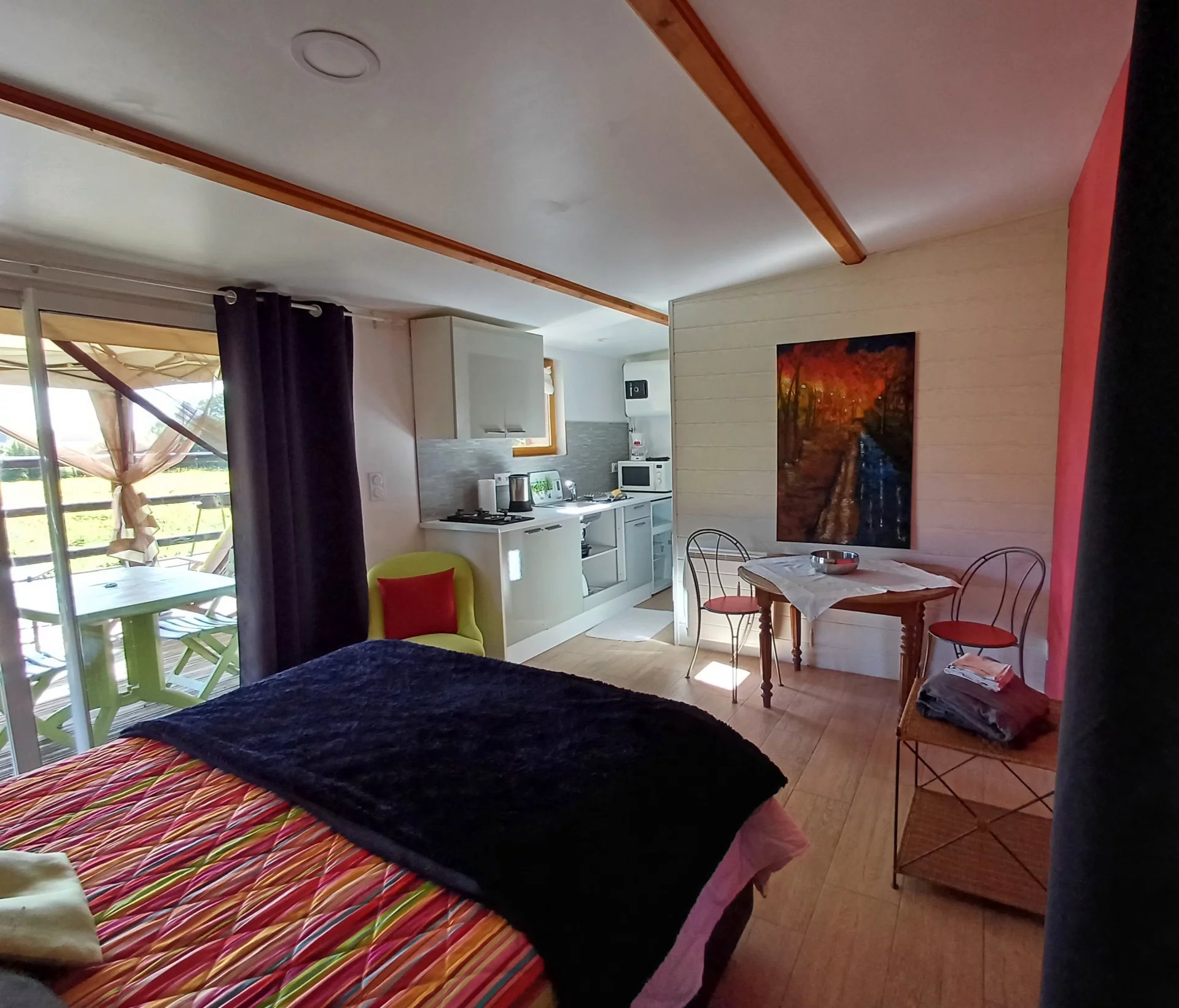 Intérieur d'un logement avec cuisine et coin salon, vue sur un jardin.
