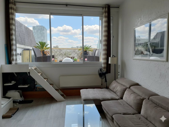 Intérieur d'un duplex lumineux avec canapé et grande fenêtre offrant une vue sur des bâtiments modernes.
