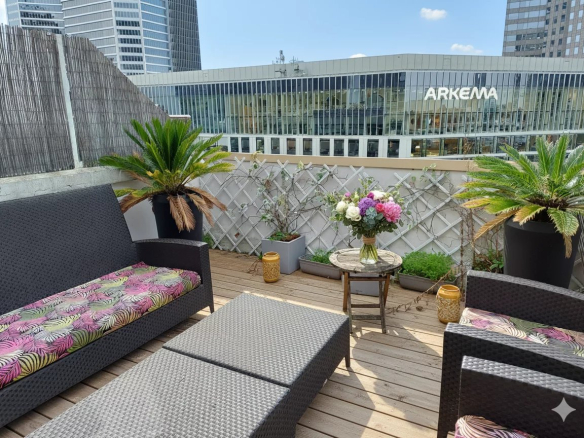 Terrasse d'un duplex avec mobilier en rotin et plantes, vue sur des bâtiments modernes à Courbevoie.