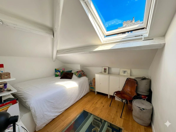 Chambre mansardée avec lit, bureau et fenêtre de toit, parquet en bois.