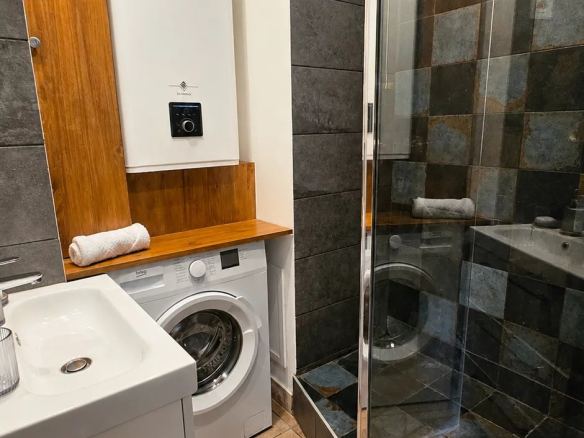 Salle de bain rénovée avec douche, lave-linge et meuble vasque.