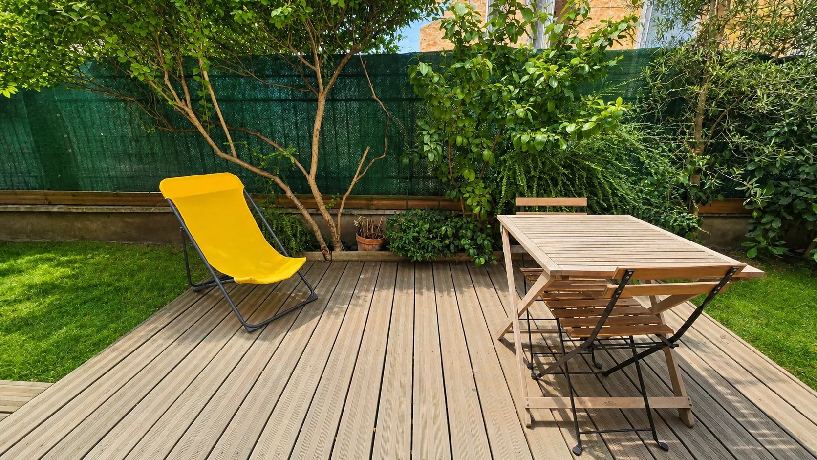 Jardin privatif arboré avec mobilier en bois et chaise longue, situé à Paris 18ème.