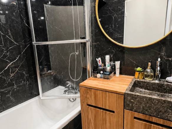Salle de bain moderne avec baignoire, douche et meuble en bois dans un appartement rénové.