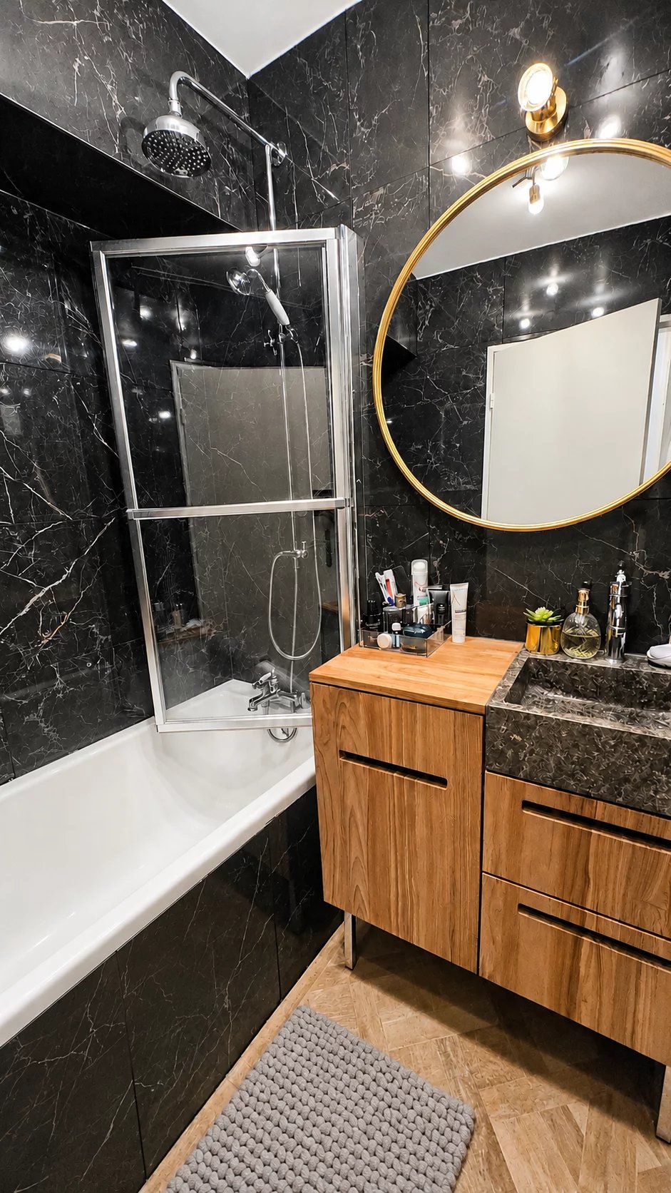 Salle de bain moderne avec baignoire, douche et meuble en bois dans un appartement rénové.