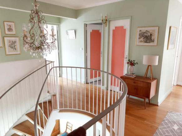 Intérieur d'un duplex à Courbevoie avec un escalier en colimaçon et des murs peints en vert pâle.