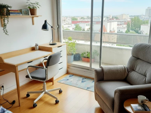 Intérieur d'un duplex à Courbevoie avec un bureau, un fauteuil et une vue sur la ville.