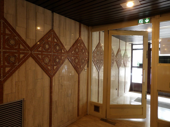 Entrée d'un immeuble avec des murs décorés de motifs géométriques en faïence.
