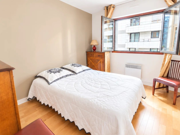 Chambre d'un appartement à Boulogne-Billancourt avec fenêtre ouverte et mobilier en bois.