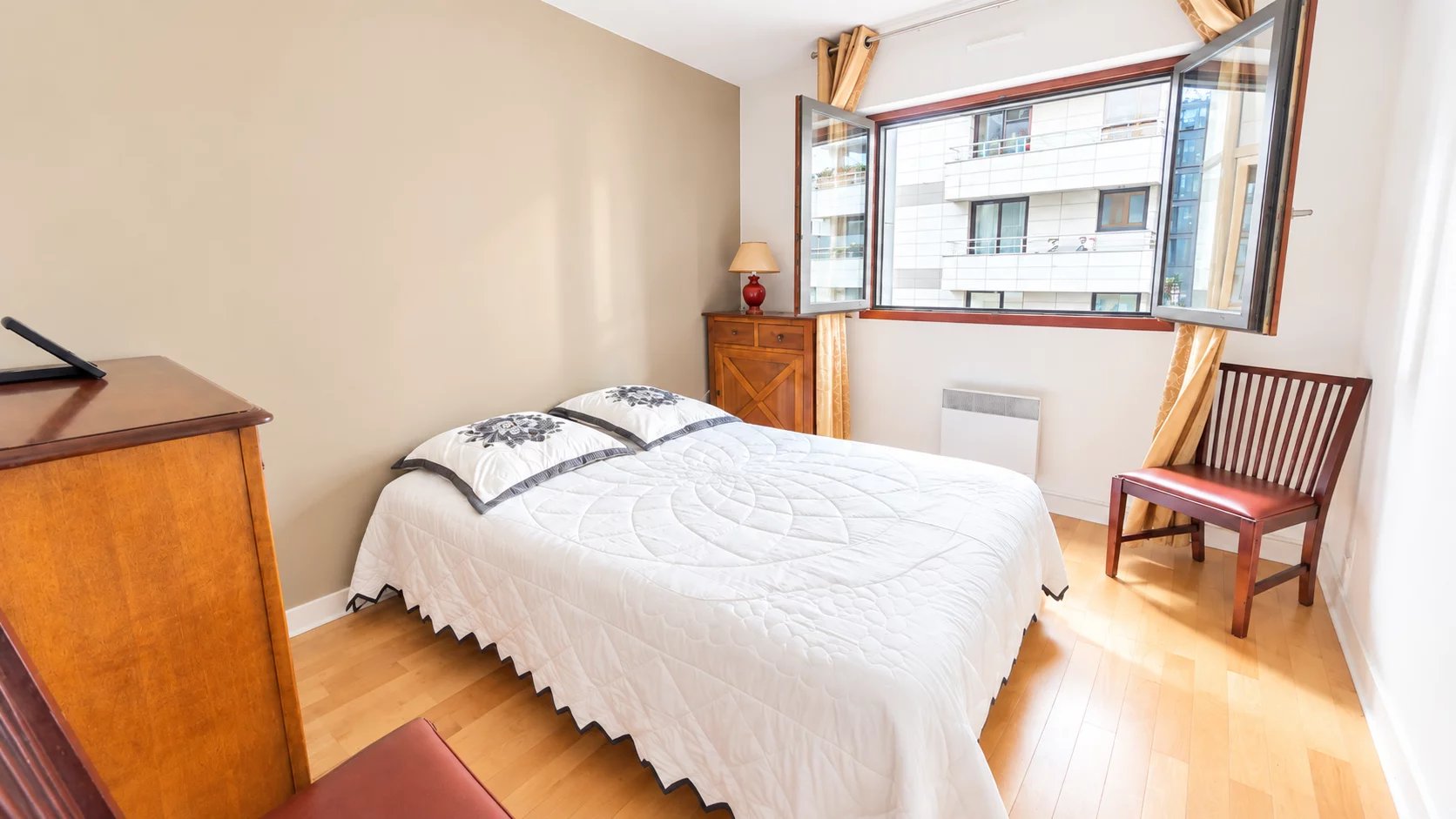 Chambre d’appartement à Boulogne-Billancourt Chambre d'un appartement à Boulogne-Billancourt avec fenêtre ouverte et mobilier en bois.