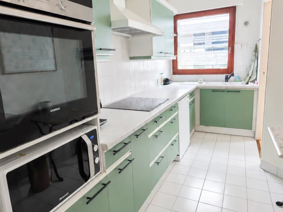 Cuisine moderne avec meubles verts et équipements électroménagers intégrés.