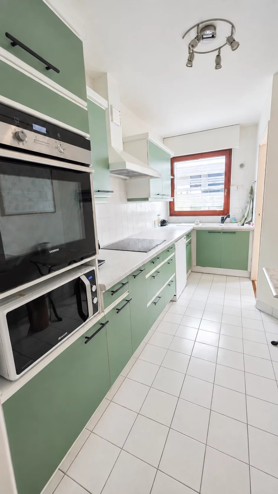 Cuisine d’un appartement à Boulogne-Billancourt Cuisine moderne avec meubles verts et équipements électroménagers intégrés.