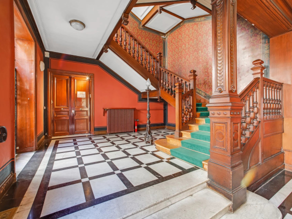 Hall d'entrée d'un immeuble en pierre de taille avec escalier en bois et sol en marbre