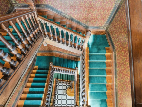 Escalier en bois avec rampe, moquette verte et murs décorés dans un immeuble ancien à Paris 17ème.