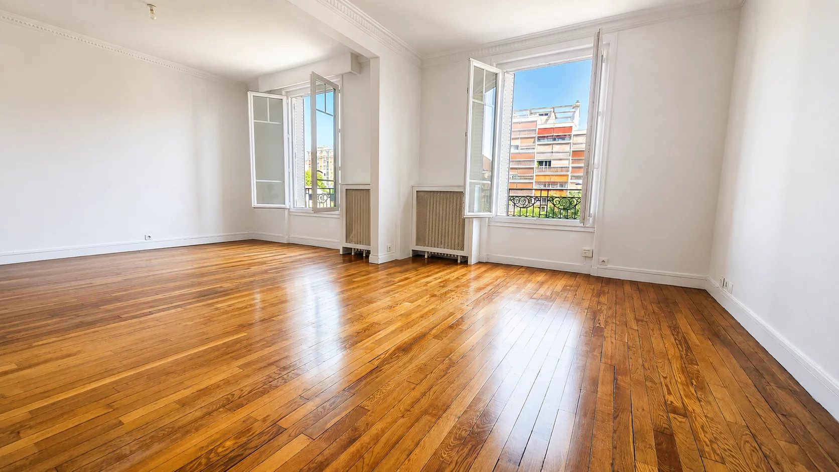 Intérieur d'un appartement rénové avec parquet, fenêtres ouvertes laissant entrer la lumière.