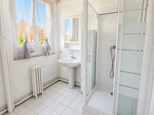 Salle de bain moderne avec douche et lavabo, fenêtres laissant entrer la lumière naturelle.