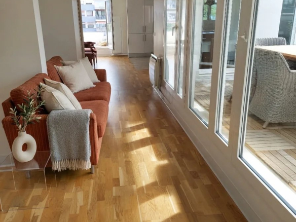 Intérieur d'un appartement spacieux avec parquet en bois, canapé et grandes fenêtres.