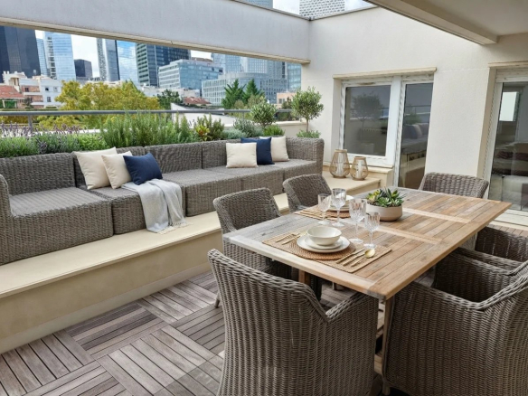 Terrasse d'un appartement avec mobilier en osier et vue sur des immeubles modernes à Courbevoie.