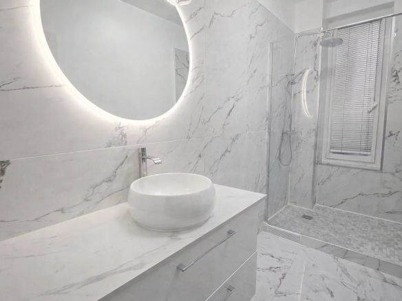 Modern bathroom with shower and marble sink, circular lighting.