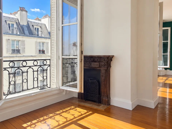 Interior of a bright apartment with parquet flooring and windows open to the blue sky.