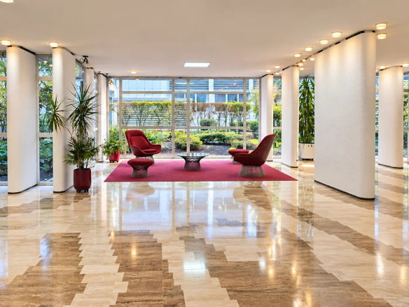 Entrance hall of a modern condominium with red armchairs and a garden visible outside.