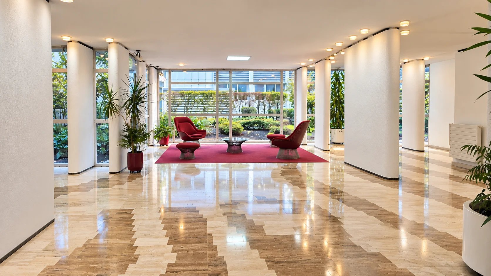 Entrance hall of a condominium in the 16th arrondissement of Paris Entrance hall of a modern condominium with red armchairs and a garden visible outside.