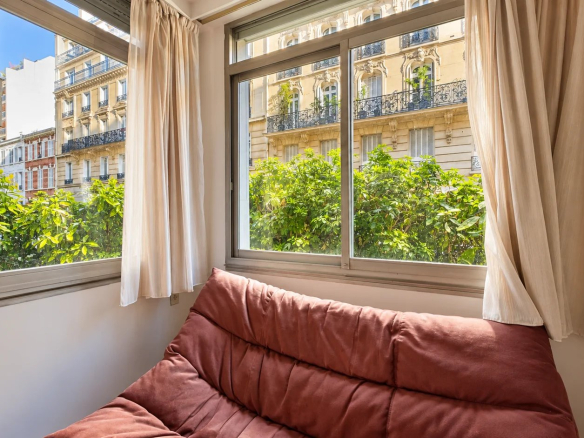 Interior view of an apartment with a sofa and windows overlooking a garden.