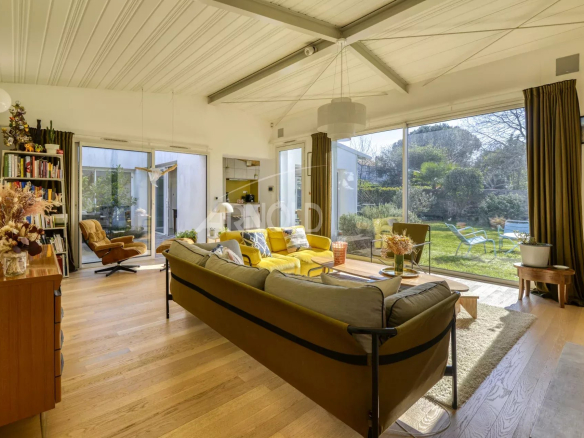 Bright living room with a yellow sofa and gray cushions, large glass doors opening to a green garden outside.