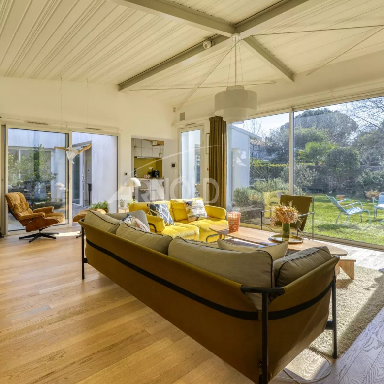 Bright living room with a yellow sofa and gray cushions, large glass doors opening to a green garden outside.
