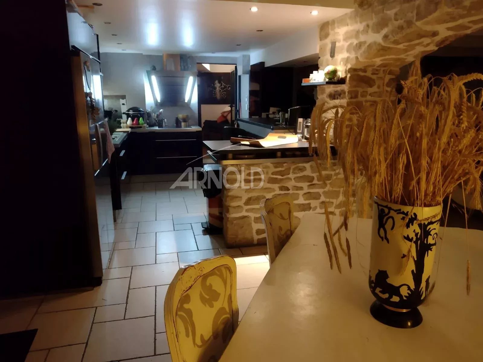 Open-plan kitchen with a stone wall, island, and a white table topped by a vase of dried wheat.