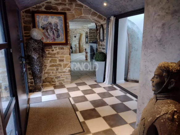 Stone-walled entry with a black-and-white checkerboard floor, framed artwork on the left, and sculptural figures near the doorway.