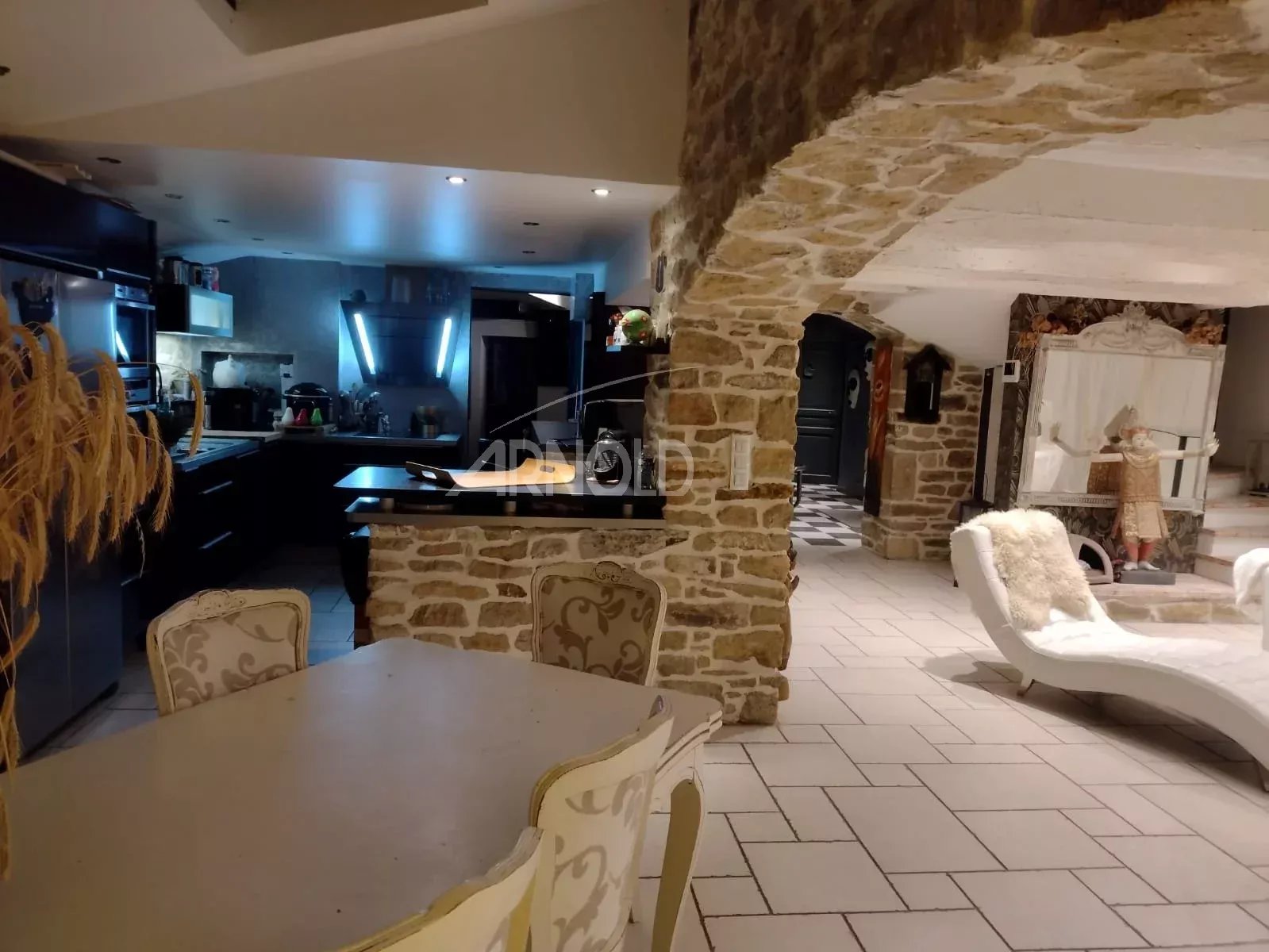 Open-plan kitchen and living area with rustic stone arches, white furniture, and a curved lounge chair.