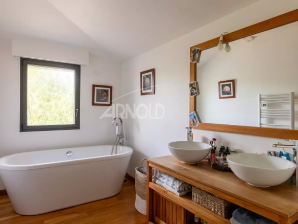 Modern bathroom with bathtub and double sink, natural light through the window.