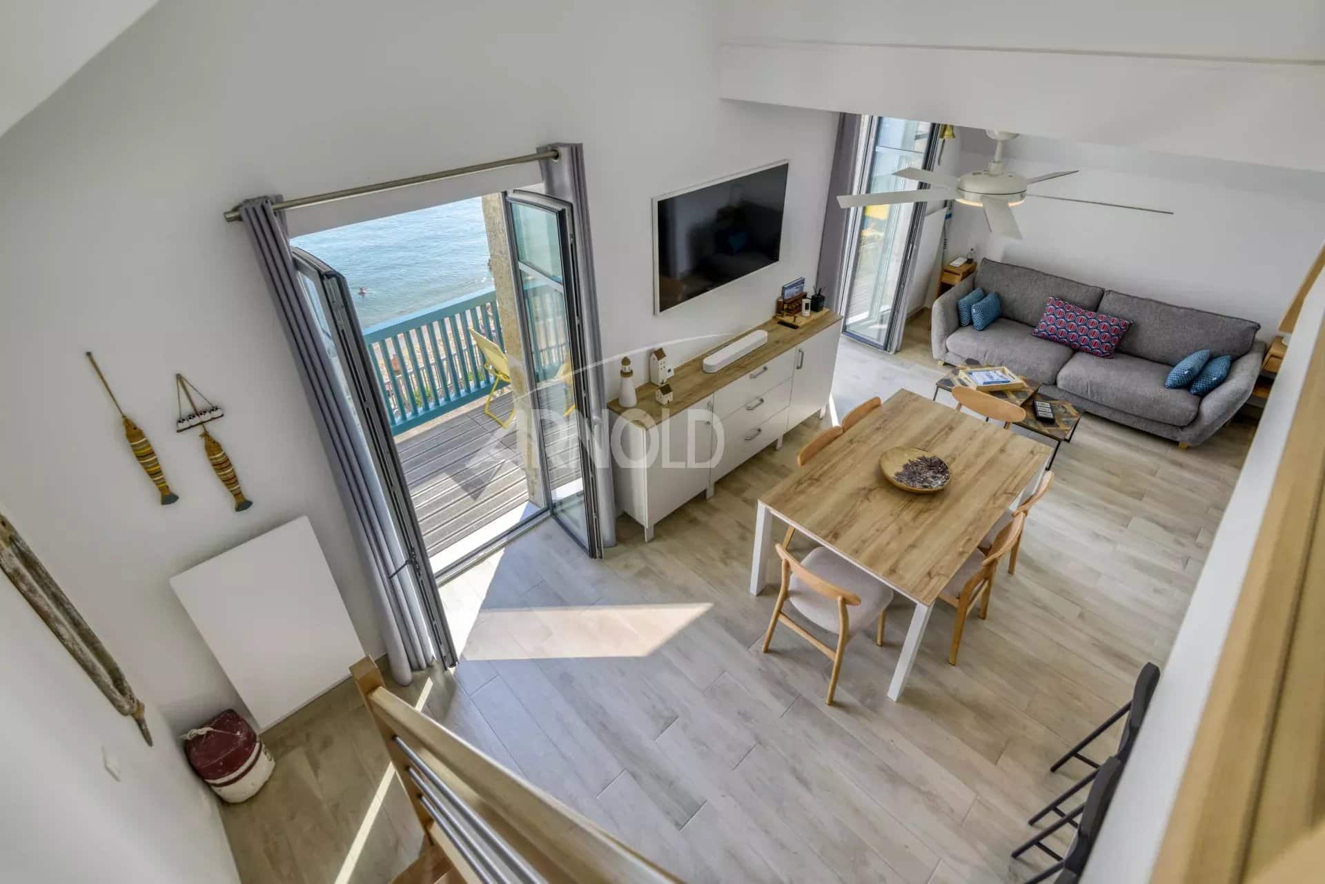 Intérieur d'un appartement en duplex avec vue sur la mer, salon lumineux et espace repas.