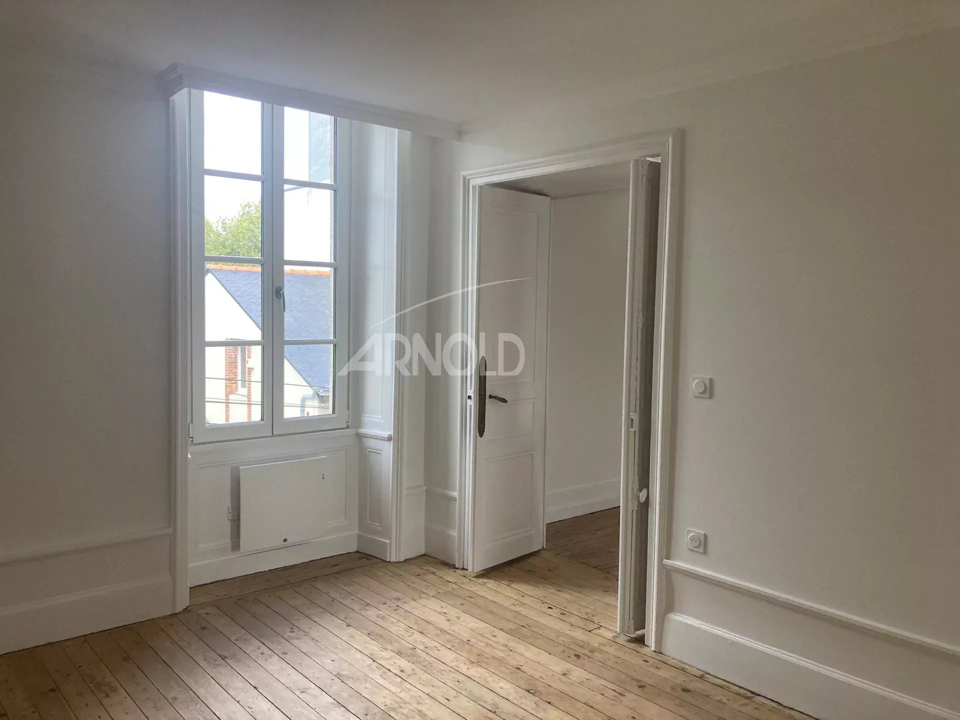 Interior of a renovated apartment with parquet flooring, bright windows and white walls in Vannes.