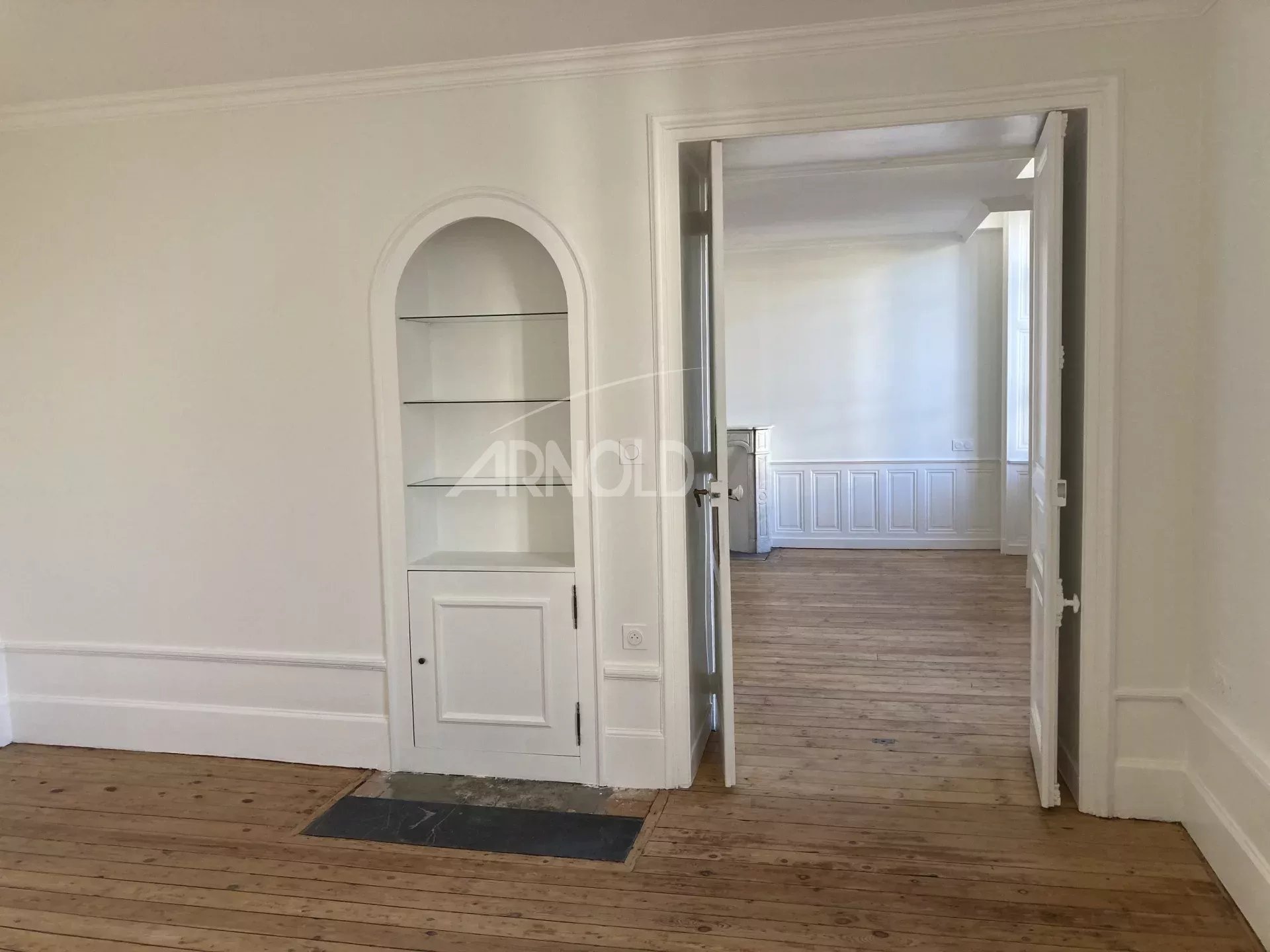 Interior of a renovated apartment with wooden parquet flooring and light walls, showing an open room.