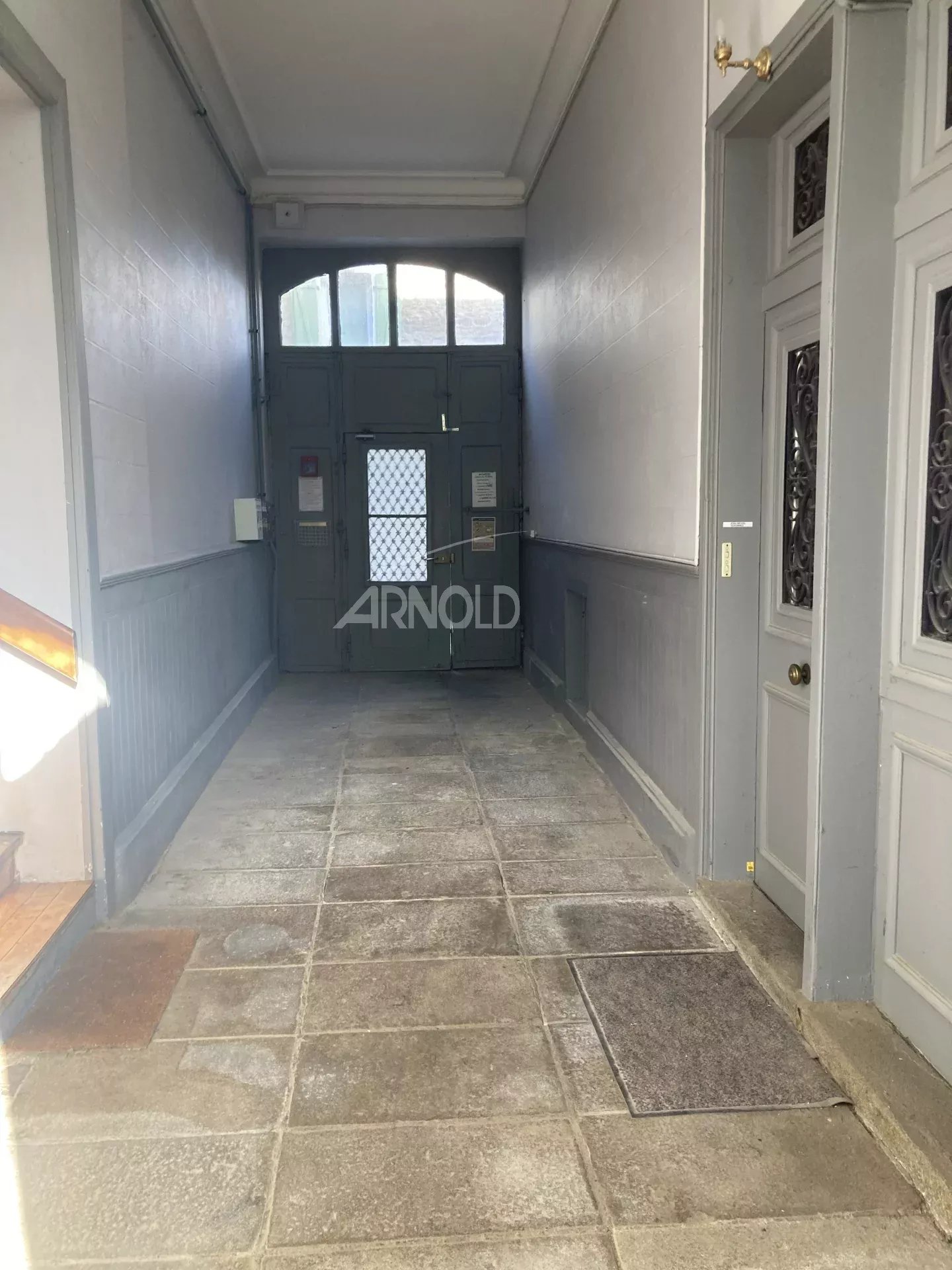 Entrance to an old building with a stone floor and grey-painted walls.