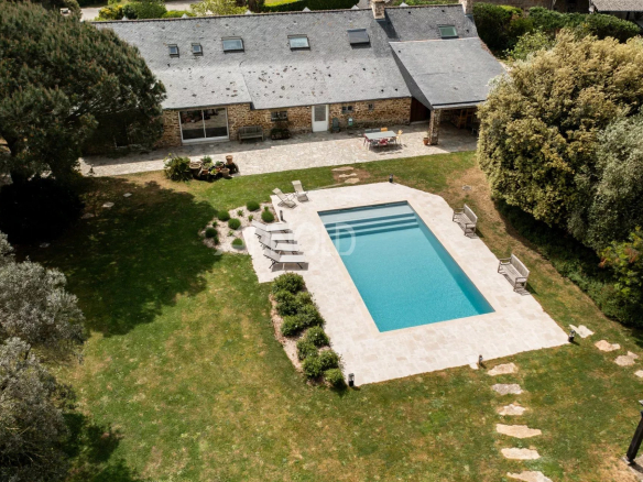 Aerial view of a stone farmhouse with swimming pool and wooded garden in Baden.