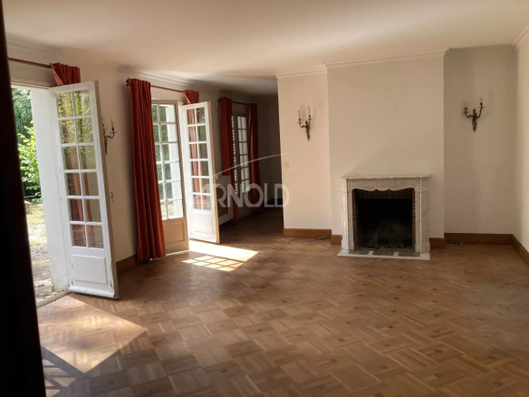 Intérieur lumineux d'une maison avec cheminée et grandes fenêtres, parquet au sol.