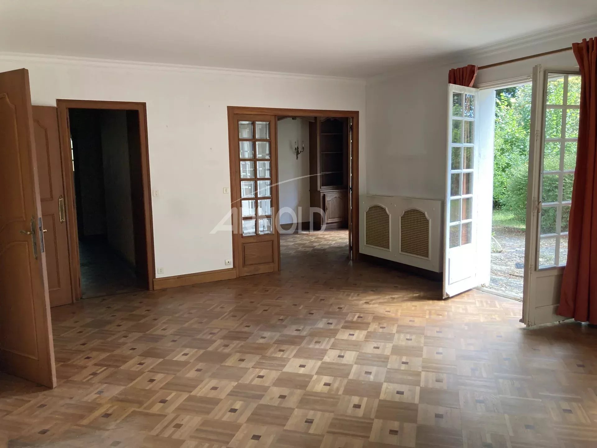 Intérieur d'une maison spacieuse avec parquet et fenêtres donnant sur un jardin arboré.