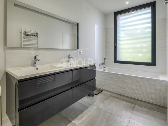 Modern bathroom with bathtub and double sink, light walls and window.