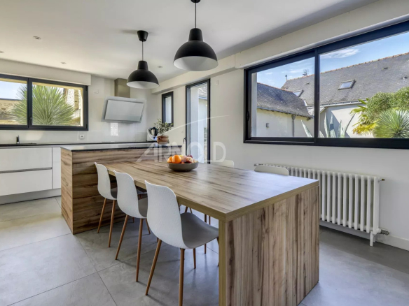 Modern kitchen with wooden table and white chairs, windows overlooking the outside.