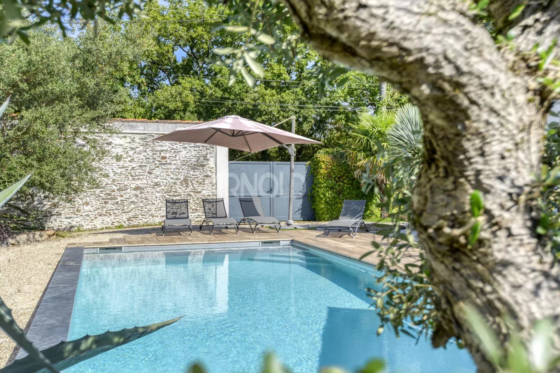 House with swimming pool in Nantes Swimming pool surrounded by sun loungers and trees, with a house in the background.