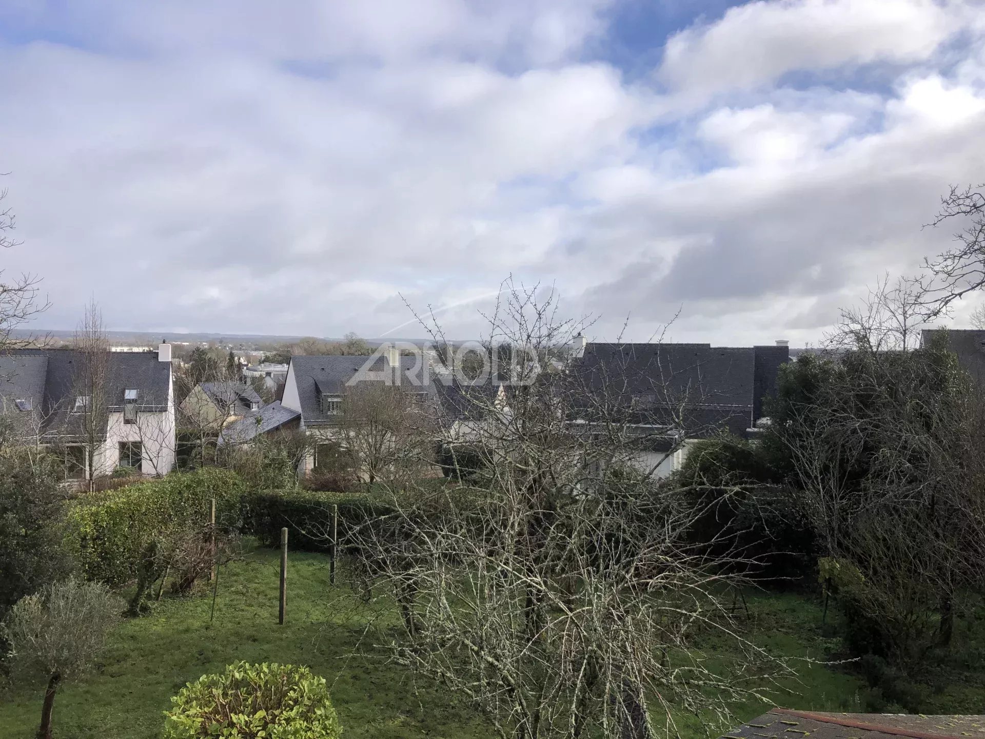 Terrain constructible à Vannes Vue d'un terrain à Vannes avec des maisons et des arbres, ciel nuageux.